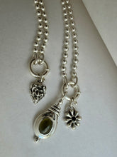Load image into Gallery viewer, A silver beaded necklace with three charms: a devil head pendant, a potion vial pendant with a green stone, and a flower charm, displayed on a light gray surface.