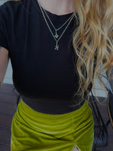 Load image into Gallery viewer, A close-up of a person wearing a black short-sleeve top and a bright yellow-green velvet wrap skirt, accessorized with layered silver necklaces.