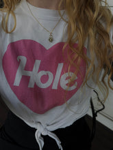 Load image into Gallery viewer, A close-up of a person wearing a white t-shirt with a large pink heart graphic and the word 'Hole' printed in white across it, tied at the waist.
