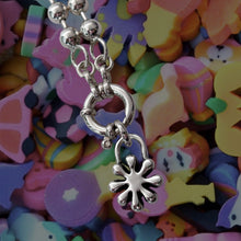 Load image into Gallery viewer, Silver necklace with a flower charm against a colorful background of kids erasers
